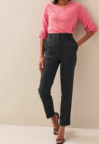 Maglione rosa a maniche lunghe abbinato a pantaloni tailored grigio scuro a vita alta. I pantaloni presentano tasche laterali e orli arrotolati. Tacchi neri con fasce.