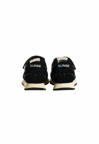 Sneaker in suede nero con suola in gomma beige. Le caratteristiche includono colletto imbottito, logo sul tallone e borchie decorative sui lati.