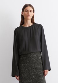 Black long-sleeve blouse with a round neckline, made of smooth fabric. Worn with a textured dark skirt featuring a subtle pattern.