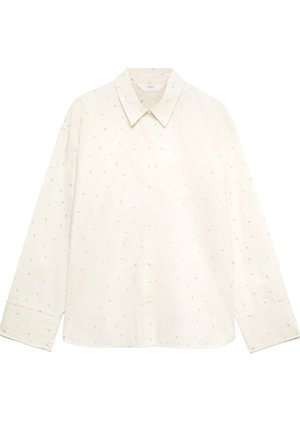 Donna con capelli ricci legati indietro che indossa una camicia bianca a maniche lunghe e morbida e pantaloncini abbinati con piccoli motivi floreali, vista di spalle.