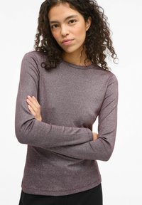 Camisa de mangas largas en púrpura oscuro con un ligero brillo. Tejido suave con un diseño ajustado y cuello redondo, sin patrones visibles.