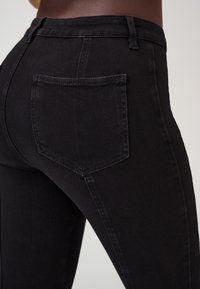 Zwarte denim jeans met een gladde textuur, voorzien van een achterzak, hoge taille en een getailleerde pasvorm die de vormen van het lichaam accentueert.