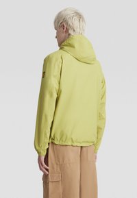 Limegrüner Kapuzenjacke mit elastischen Bündchen und Saum, die eine schlanke Stofftextur und ein Logopatch am Ärmel hat.