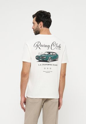Mężczyzna z ciemnymi włosami i brodą zwrócony tyłem, ubrany w białą koszulkę z nadrukiem vintage zielonego samochodu i napisem "Racing Club L.A. California Team" na plecach.