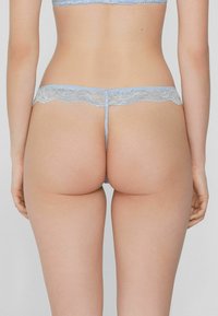 Hellblaue Spitzenhose mit breitem Spitzenband und dünnen Trägern, verziert mit einem floralen Muster und verstellbaren Seiten. Glatte Stoffstruktur.
