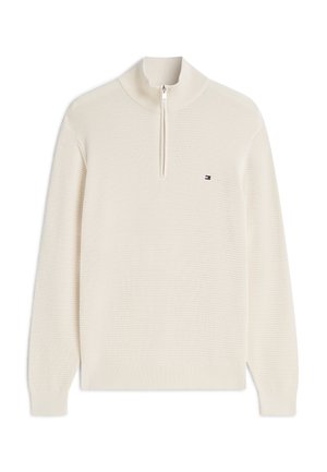 Kremfarvet, strikket pullover med lange ærmer, halv lynlåsåbning ved kraven og en lille rektangulær logo på venstre bryst.