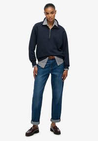 Marine sweater met een kwart rits, gestreept shirt eronder, blauwe jeans en bordeauxrode instappers. Casual gelaagde outfit.