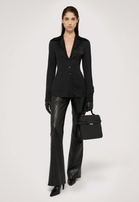 Černá dlouhá blůza s hlubokým V-výstřihem, v kombinaci s přiléhavými černými koženými kalhotami a elegantními černými podpatky, držící strukturovanou černou kabelku.