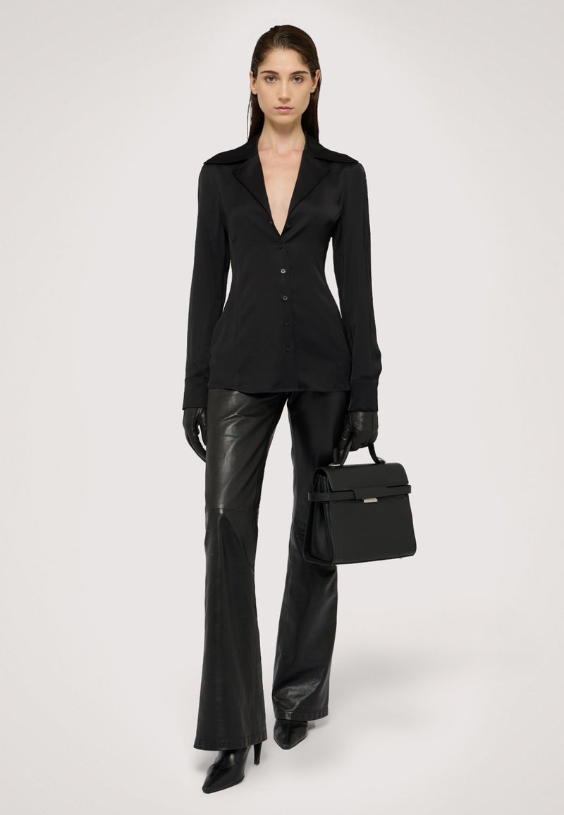 Černá dlouhá blůza s hlubokým V-výstřihem, v kombinaci s přiléhavými černými koženými kalhotami a elegantními černými podpatky, držící strukturovanou černou kabelku.