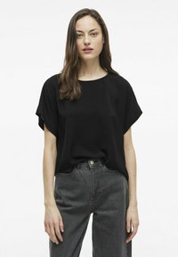 Juodas trumpomis rankovėmis viršus su apvaliu iškirpimu, pagamintas iš lengvo tekstūruoto audinio; derinamas su aukštu liemeniu tamsiais džinsais. 