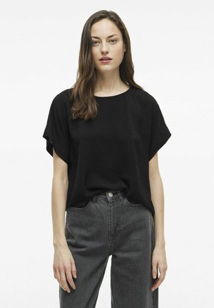 Sort kortærmet top med rund hals, lavet af let tekstureret stof; parret med højtaljede mørke denimjeans.