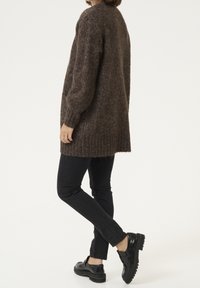 Brązowy sweter dziergany o luźnym kroju, z prążkowanym dołem i mankietami. W połączeniu z czarnymi, dopasowanymi dżinsami i czarnymi butami na platformie.