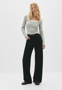 Haut gris à manches longues avec encolure arrondie, associé à un pantalon noir taille haute et coupe large. Le mannequin porte des chaussures à finition brillante.