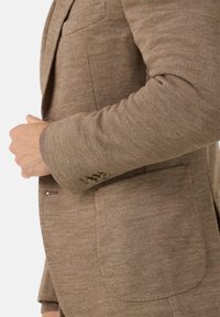 Hnědý sak na míru vyrobené z texturované látky, s klopou, jednobotonovým zapínáním a náprsní kapsou.