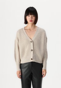 Beige pletený kardigan s výstřihem do V, předním zapínáním na knoflíky a krátkým střihem. Měkká textura a ribovaný vzor vytvářejí uvolněný střih.