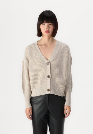 Cardigan en tricot beige avec un col en V, fermeture par boutons à l'avant et design court. La texture douce et le motif côtelé créent un ajustement décontracté.