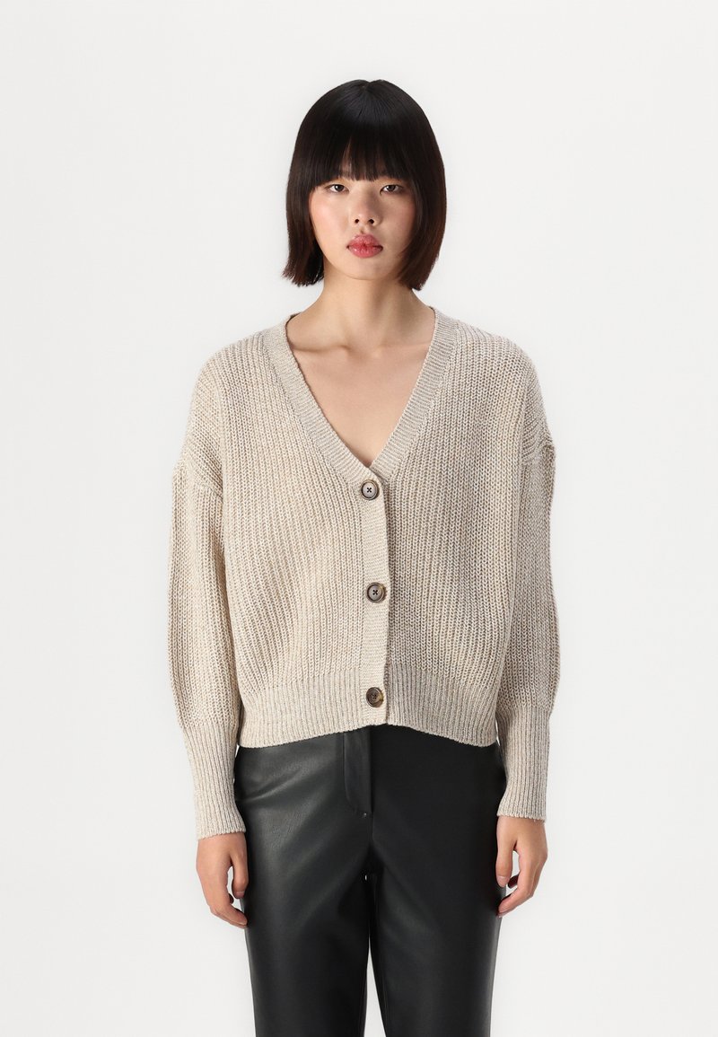 Beige pletený kardigan s výstřihem do V, předním zapínáním na knoflíky a krátkým střihem. Měkká textura a ribovaný vzor vytvářejí uvolněný střih.
