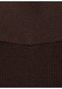 Gros plan sur un tissu tricoté brun foncé montrant deux motifs de tricot distincts avec une couture horizontale séparant les textures.