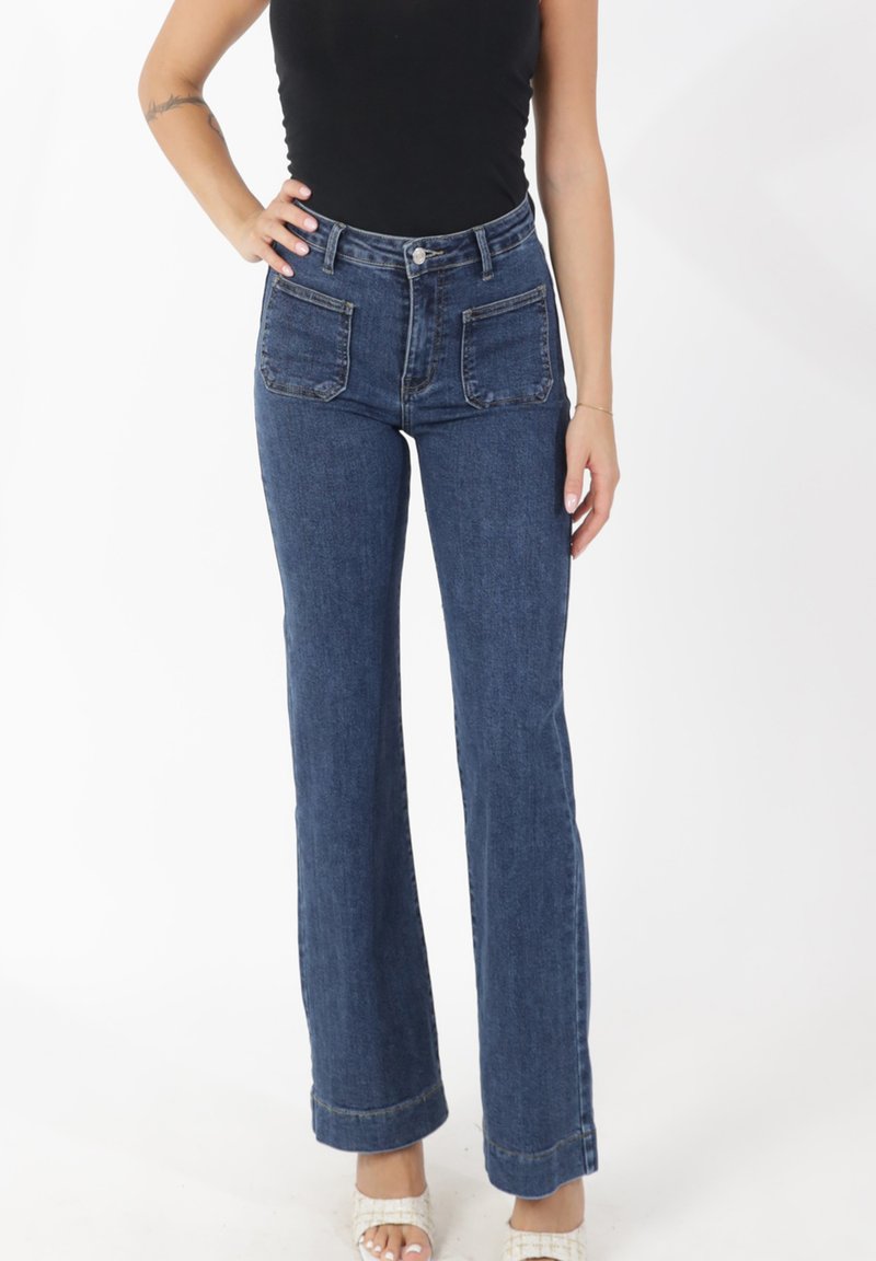 Jeans de mezclilla de tiro alto y con campana en azul oscuro. Incluyen bolsillos delanteros y traseros, detalles cosidos y un corte recto desde la rodilla hasta el dobladillo.