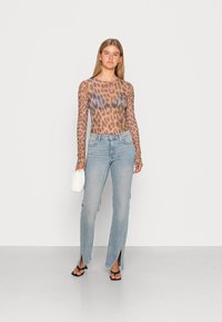 Top com mangas compridas, de tecido transparente, estampado com padrão de leopardo e com um design ajustado, combinado com jeans azul claro com bainhas abertas, complementado por uma bolsa branca.