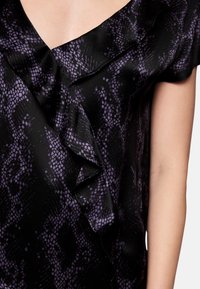 Black top with purple snake print, featuring a v-neckline and a ruffle detail along the front, made from a smooth satin-like fabric.