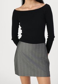 Zwarte ribbeltrui met een off-the-shoulder halslijn, gecombineerd met een minirok in grijze krijtstreep. De rok heeft een aansluitende silhouet en een zijsplit.