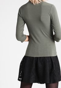 Olive green ribbed long-sleeve top with a round neckline, paired with a black lace skirt featuring a flared design and decorative accents.