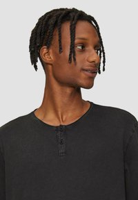 Czarna koszula z długim rękawem o okrągłym dekolcie, z zapięciem na dwa guziki i fakturowanym materiałem. Charakteryzuje się luźnym krojem i subtelnymi detalami w szwie.