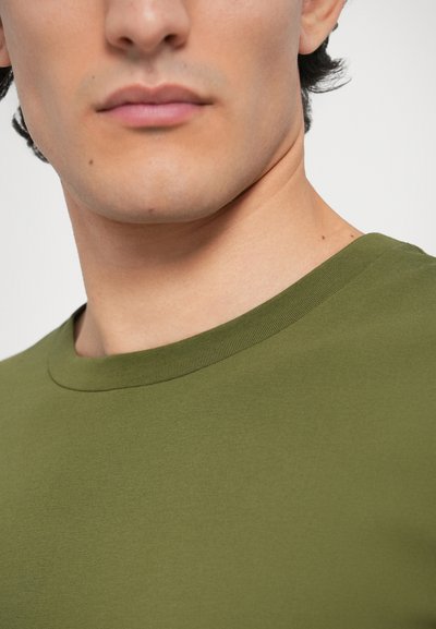 Λαδί πράσινη κοντομάνικη μπλούζα με στρογγυλή λαιμόκοψη, κατασκευασμένη από μαλακό βαμβάκι. Διαθέτει λεία υφή και εφαρμοστή γραμμή χωρίς ορατά μοτίβα ή διακοσμητικά στοιχεία.