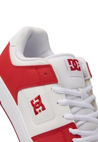 Zapatilla blanca con acentos de cuero rojo, que presenta un cuello acolchado, cordones blancos y un logotipo rojo en el lado exterior. Textura suave en general.