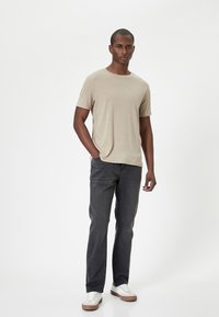 Camiseta beige de manga corta combinada con jeans gris oscuro. Zapatillas de lona con parte superior crema y suela beige. Diseño simple y casual.