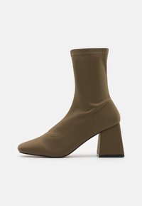 Beżowy botek za kostkę z elastyczną cholewką, szpiczastym noskiem i masywnym kwadratowym obcasem. Przeszycia wzdłuż boków dodają faktury.
