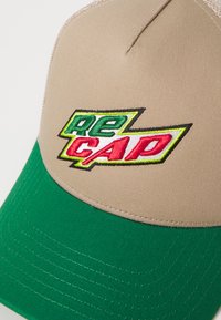 Beige színű baseball sapka zöld szélekkel, piros és zöld hímzett "RE CAP" logóval. Simított anyag, látható varrásokkal.