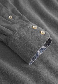 Grauer Stoffhemdmanschette mit zwei gelben Knöpfen, ausgestattet mit einem blütenförmigen Innenfutter in Blau und Weiß. Weiche Textur und taillierter Schnitt.