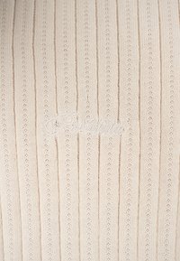 Tissu tricoté côtelé couleur crème avec des rayures verticales subtiles et un mot en écriture cursive brodé discrètement au centre.