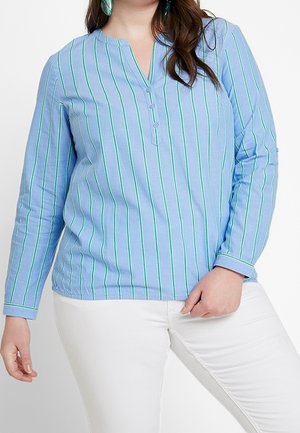 Camisa de manga larga azul claro con rayas verdes verticales, un cuello henley y tres botones en el frente, combinada con pantalones blancos.