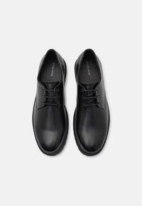 Chaussures en cuir noir à finition lisse, bout rond, design à lacets, semelles en caoutchouc, avec un marquage discret sur la semelle intérieure.