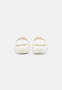 Vita slip-on sandaler med öppen baksida, rund tå och slät textur. Har en minimalistisk design och ingen synlig hårdvara.