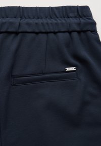 Marina blå joggers i mjukt tyg har ett elastiskt midjeband och en bakficka med en silvertagg märkt "CECIL." Slät textur, enkel design.