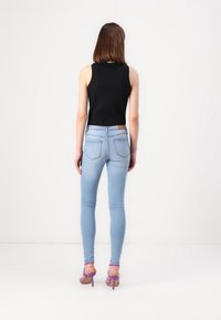 Černý top bez rukávů spojený s bledě modrými úzkými džíny. Džíny mají střední pas, pět kapes a hnědou etiketu na zadní straně.