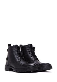Botas de cuero negro con un acabado texturizado, cordones en la parte delantera, cremallera lateral y suela de goma resistente con patrones de pisada pronunciados.