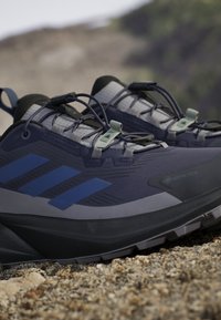 Scarpe da corsa blu navy con parte superiore in Gore-Tex, materiale testurizzato e tre strisce blu di lato. Include lacci elastici e suola in gomma.