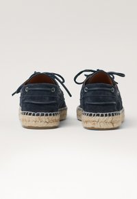 Chaussures en daim bleu marine avec un design à lacets, semelles en jute espadrille et coutures contrastées. Texture lisse, bout rond et accents minimalistes.
