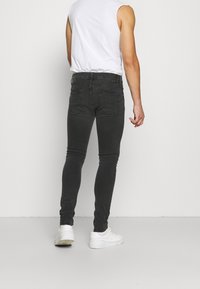 Černé úzké džíny vyrobené z džínoviny s hladkým povrchem, s zadními kapsami a vysokým pasem, doplněné bílým bezrukávovým topem.