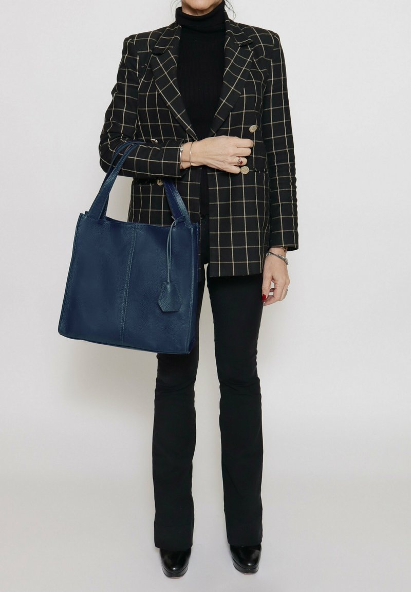 Borsa a spalla in pelle blu navy con due manici robusti, forma rettangolare, superficie liscia e un'etichetta decorativa sul lato.