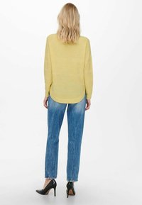 Pull jaune pâle en maille côtelée avec un ourlet arrondi. Associé à un jean droit bleu délavé et des chaussures noires à talons hauts.