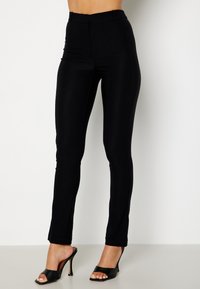 Leggings neri a vita alta realizzati in materiale elastico con un design elegante. Presentano una silhouette aderente e dettagli sottili sulle cuciture laterali.