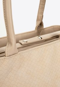 Beige handtas met een gestructureerd, schubachtig patroon. Voorzien van twee zachte handvatten en een magnetische drukknoopsluiting aan de bovenkant voor een veilige sluiting.
