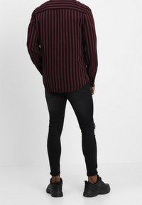 Men's long-sleeve shirt with vertical red and black stripes, constructed from soft fabric, paired with black fitted jeans and sneakers.