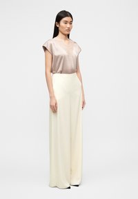 Μεταξένιο μπεζ τοπ με δαντελωτό ντεκολτέ, συνδυασμένο με υψηλόμεσα κρεμ παντελόνια φαρδιάς γραμμής. Λείος υφασμάτινος υφή και κομψός σχεδιασμός.